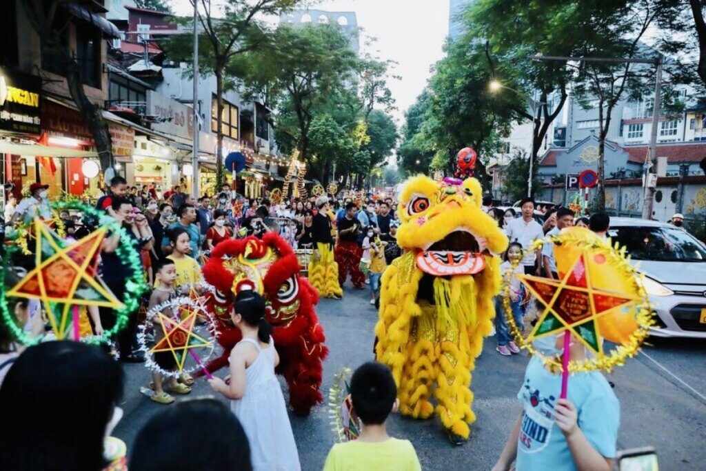 Children watching lion dance and carrying colorful lanterns during the Mid-Autumn Festival in Vietnam