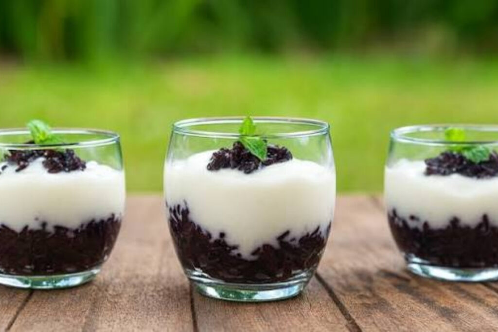 Best Vietnamese Desserts: 20 Sweet Treats Every Traveler Should Try in Vietnam 16 Vietnamese yogurt served with fermented purple sticky rice, fresh mint leaves, and roasted sesame seeds in a glass dessert bowl.