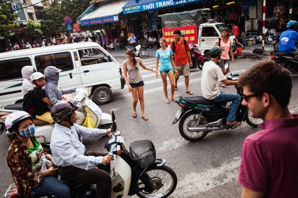 Pedestrian crossing a busy street in Hanoi surrounded by motorbikes