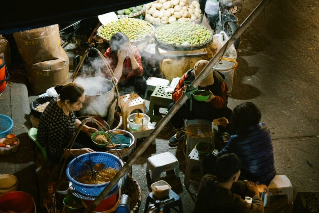 People sharing food on plastic stools at a Vietnamese street food stall
