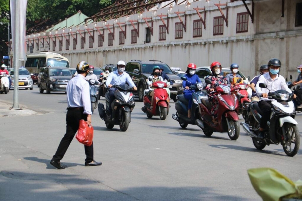 Pedestrian crossing a busy street in Vietnam while motorcycles pass nearby